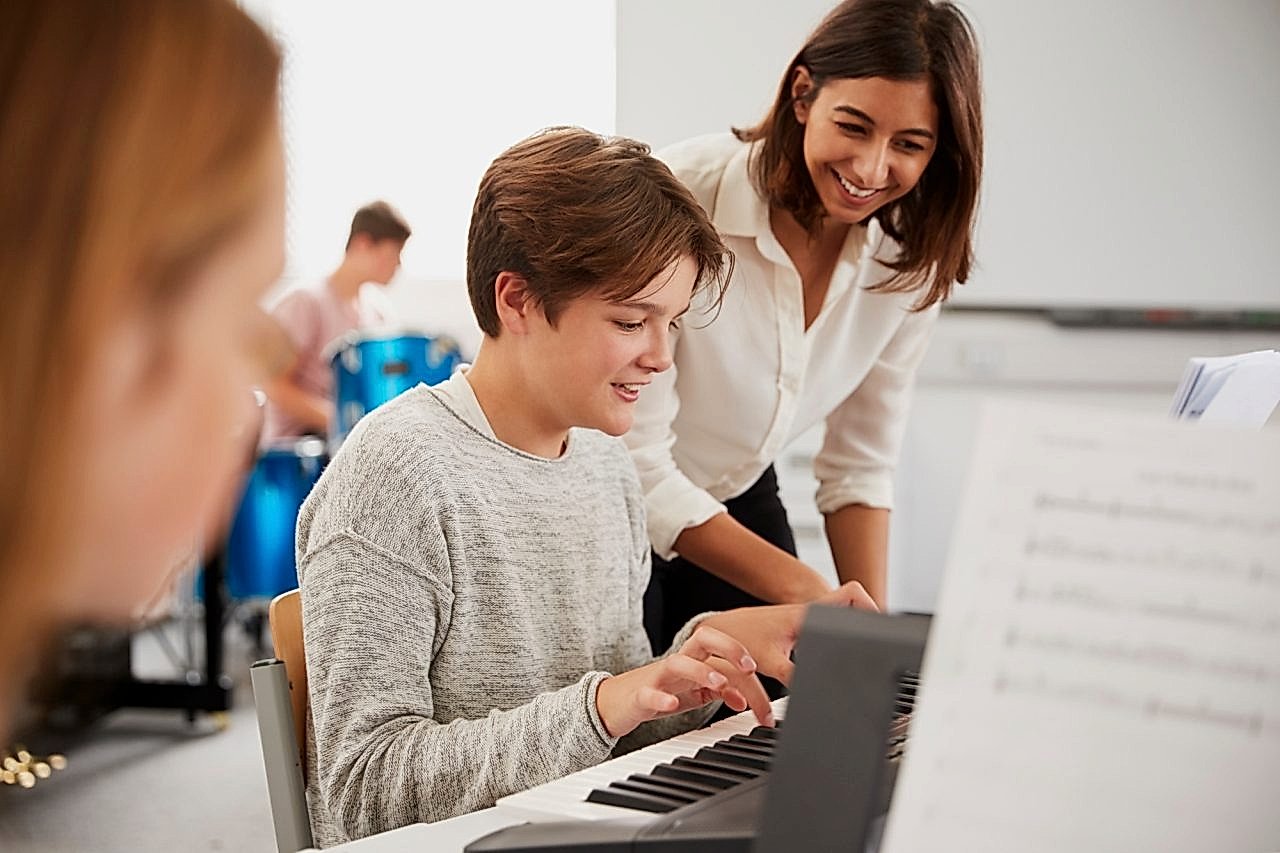 Male Pupil With Teacher Playing Piano In Music Lesson